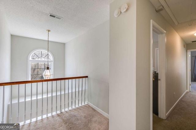 hall with attic access, baseboards, visible vents, a textured ceiling, and carpet flooring