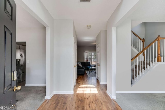 hallway featuring visible vents, stairs, baseboards, and wood finished floors