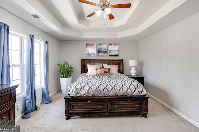 bedroom with light carpet, a tray ceiling, visible vents, and baseboards