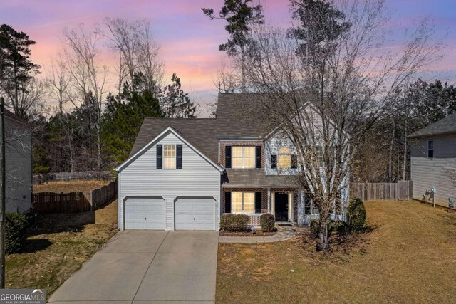 view of front of property with an attached garage, brick siding, fence, driveway, and a yard