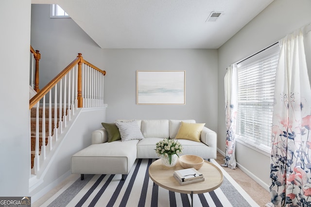 living area with carpet floors, stairway, visible vents, and baseboards