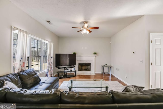 living area featuring a fireplace, wood finished floors, visible vents, baseboards, and a ceiling fan