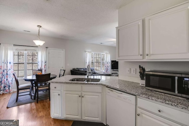 kitchen with white dishwasher, a peninsula, a sink, white cabinets, and stainless steel microwave