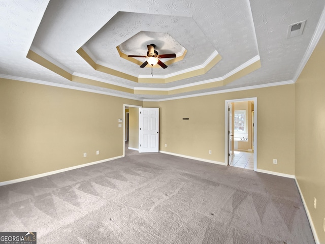 unfurnished bedroom with baseboards, visible vents, a tray ceiling, crown molding, and carpet flooring