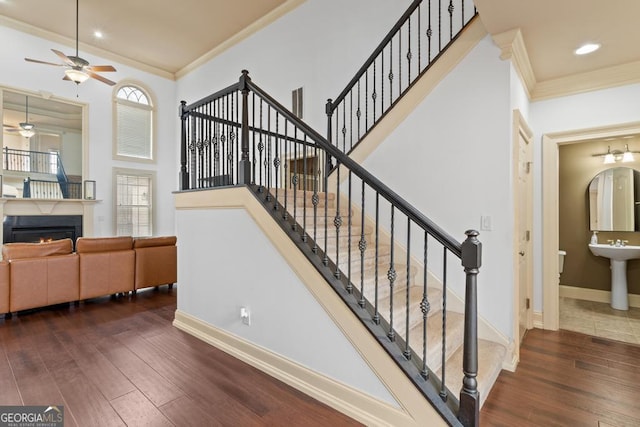 staircase with a warm lit fireplace, baseboards, wood finished floors, and crown molding