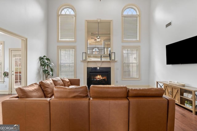 living room featuring a towering ceiling, visible vents, wood finished floors, and a glass covered fireplace