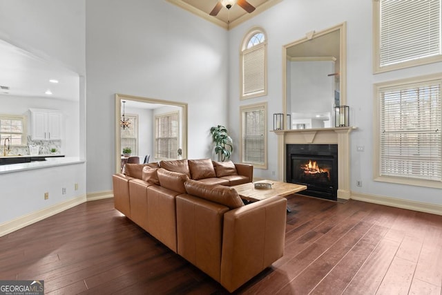 living room featuring dark wood-type flooring, a fireplace with flush hearth, a high ceiling, and baseboards