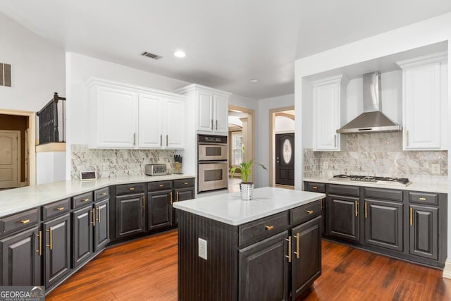 kitchen featuring stainless steel appliances, dark wood-style flooring, white cabinetry, light countertops, and wall chimney exhaust hood