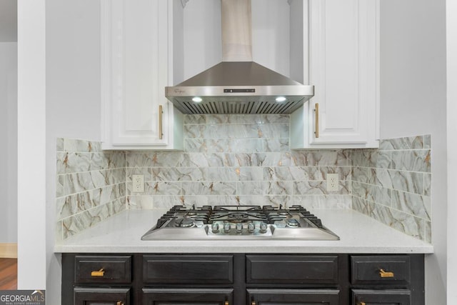 kitchen with stainless steel gas cooktop, wall chimney range hood, backsplash, and white cabinets