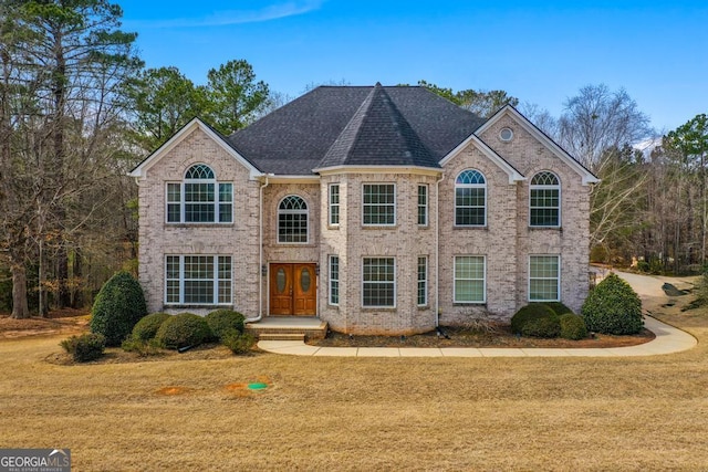 view of front of house with a shingled roof, a front yard, and brick siding