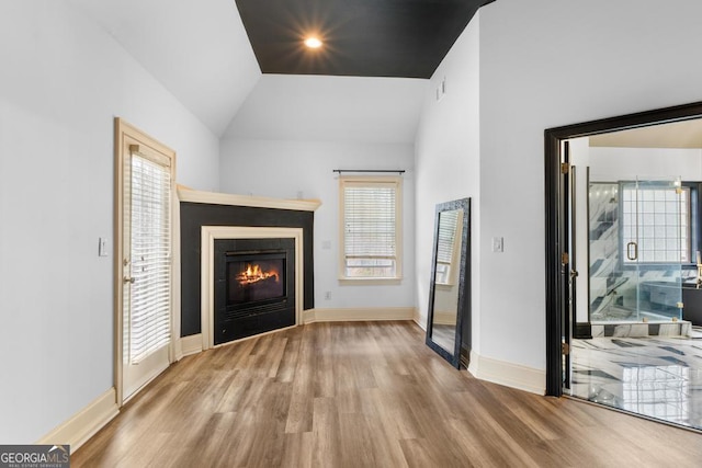 unfurnished living room with lofted ceiling, a lit fireplace, wood finished floors, and a wealth of natural light