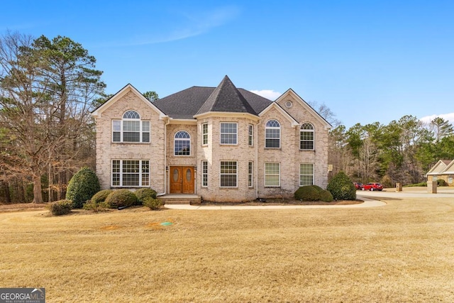 view of front of house featuring a shingled roof, a front yard, and brick siding