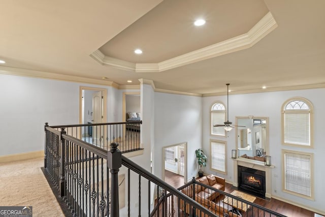 corridor featuring a tray ceiling, an upstairs landing, and a healthy amount of sunlight