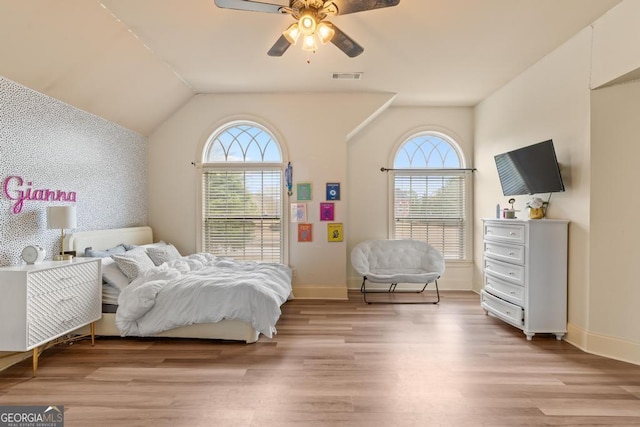 bedroom with wallpapered walls, light wood finished floors, visible vents, an accent wall, and multiple windows