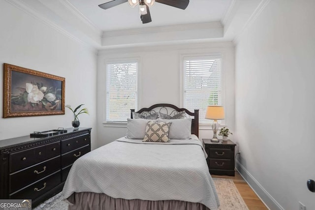 bedroom featuring ceiling fan, light wood-style flooring, baseboards, ornamental molding, and a raised ceiling