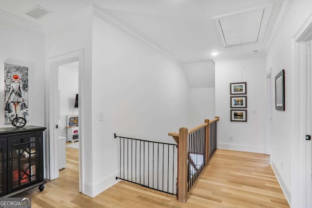 corridor with crown molding, light wood finished floors, visible vents, attic access, and an upstairs landing