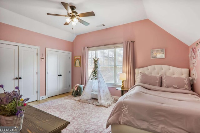 bedroom featuring visible vents, ceiling fan, wood finished floors, vaulted ceiling, and two closets