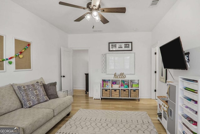 living room featuring light wood-type flooring, visible vents, and a ceiling fan