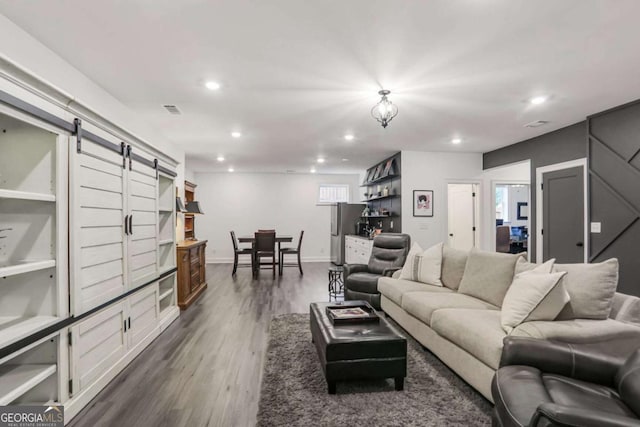 living area with recessed lighting, visible vents, a barn door, dark wood-type flooring, and baseboards