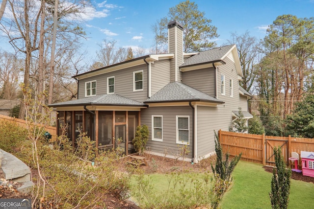 rear view of house featuring a shingled roof, a sunroom, a chimney, fence, and a yard