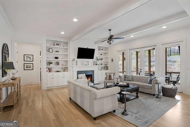 living area featuring light wood finished floors, a lit fireplace, french doors, and beam ceiling