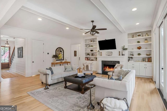 living room with light wood finished floors, a lit fireplace, stairway, and beam ceiling