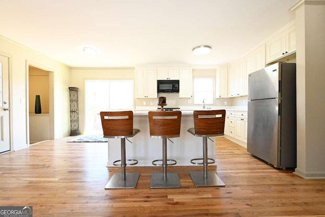 kitchen with black microwave, a breakfast bar, light countertops, freestanding refrigerator, and light wood-style floors