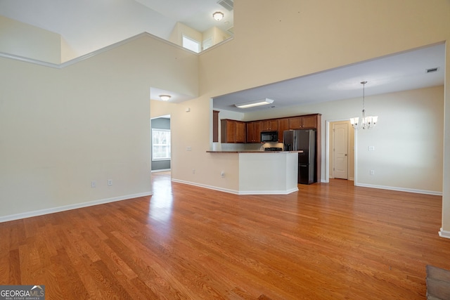 unfurnished living room with a chandelier, a high ceiling, light wood-type flooring, and baseboards