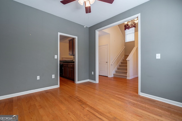 spare room with light wood finished floors, ceiling fan, stairs, and baseboards