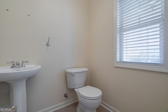 half bathroom featuring tile patterned flooring, baseboards, a sink, and toilet