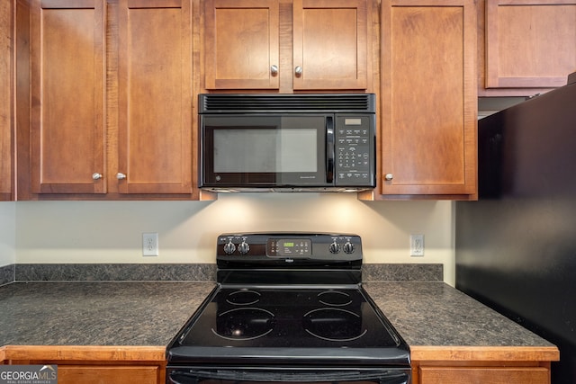 kitchen with brown cabinetry, dark countertops, and black appliances