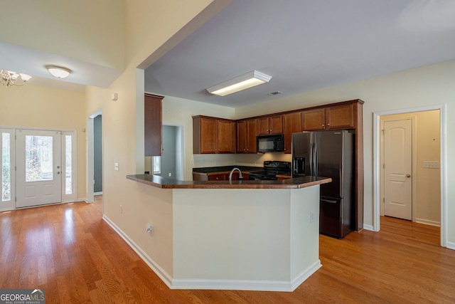 kitchen with dark countertops, black appliances, a peninsula, and light wood-style floors