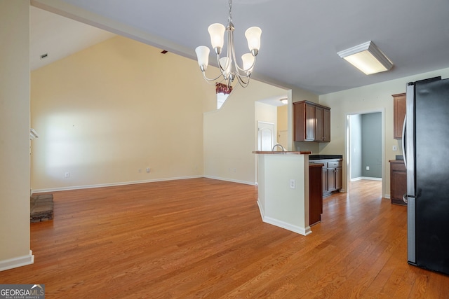 kitchen featuring a peninsula, baseboards, vaulted ceiling, light wood-style floors, and freestanding refrigerator