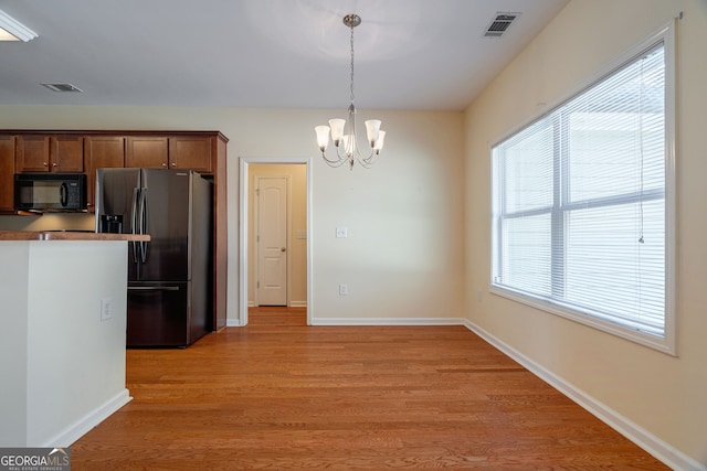 kitchen featuring light wood finished floors, baseboards, a chandelier, black microwave, and stainless steel refrigerator with ice dispenser