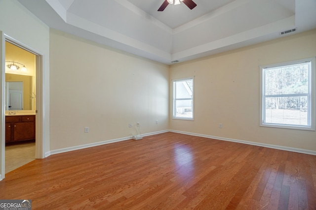 interior space with light wood-style flooring, visible vents, baseboards, a raised ceiling, and ensuite bath