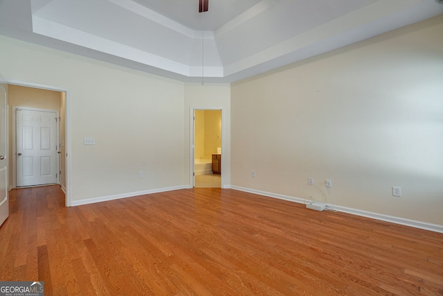 unfurnished bedroom featuring a raised ceiling, ensuite bath, light wood-style flooring, and baseboards