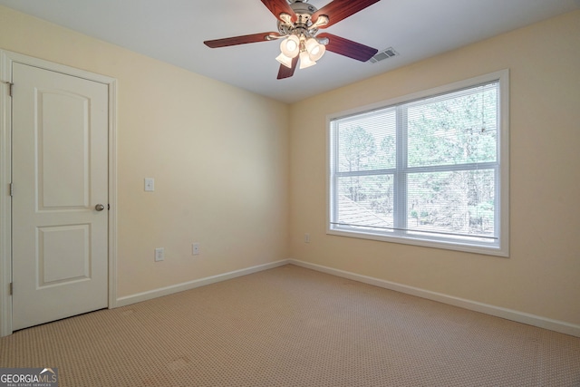 spare room featuring light carpet, ceiling fan, visible vents, and baseboards