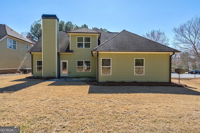 back of house featuring roof with shingles, a yard, and a chimney