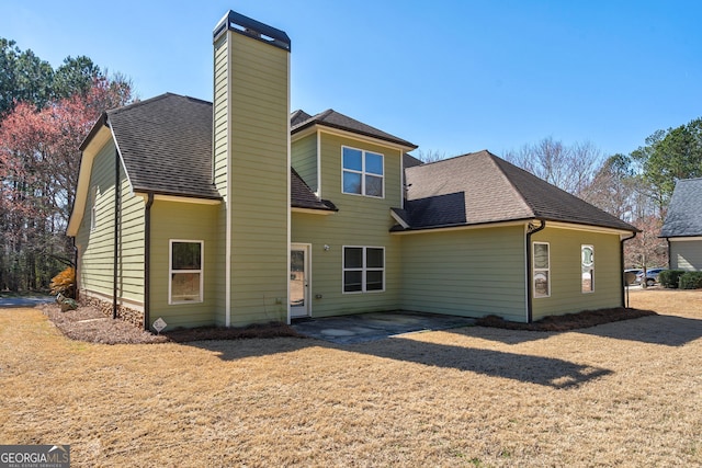 back of property with a patio, a shingled roof, a chimney, and a lawn