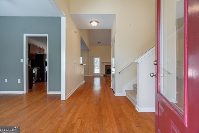 foyer entrance with light wood-type flooring, stairs, baseboards, and a fireplace with raised hearth