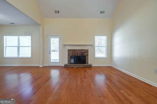 unfurnished living room featuring visible vents, a stone fireplace, baseboards, and wood finished floors