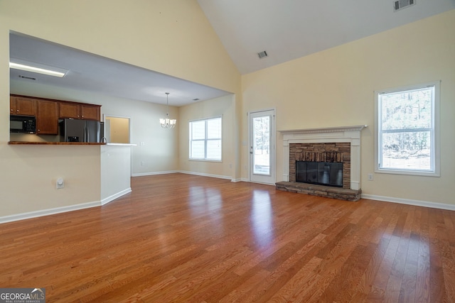 unfurnished living room with baseboards, wood finished floors, an inviting chandelier, a stone fireplace, and high vaulted ceiling