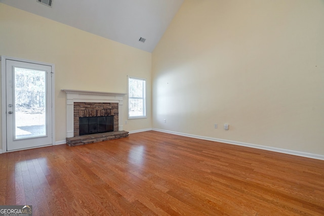 unfurnished living room featuring baseboards, visible vents, wood finished floors, a fireplace, and high vaulted ceiling