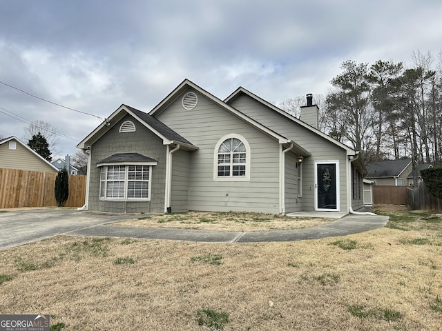 view of front of house featuring a chimney, fence, and a front lawn