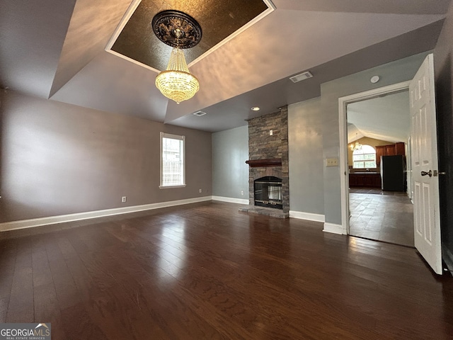 unfurnished living room with baseboards, visible vents, wood finished floors, vaulted ceiling, and a stone fireplace