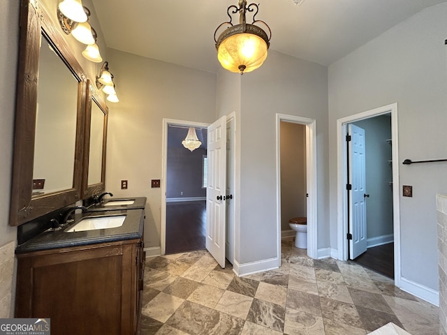 full bath featuring toilet, a sink, baseboards, and double vanity