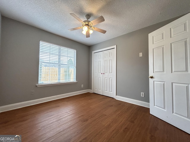 unfurnished bedroom featuring a textured ceiling, dark wood-type flooring, a closet, and baseboards