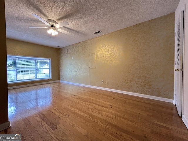 spare room featuring visible vents, a ceiling fan, a textured wall, wood finished floors, and a textured ceiling