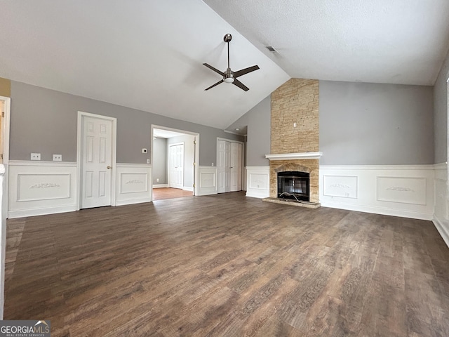 unfurnished living room featuring wainscoting, ceiling fan, dark wood-style flooring, vaulted ceiling, and a fireplace