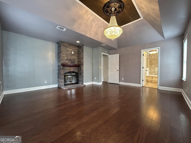 unfurnished living room featuring a stone fireplace, visible vents, baseboards, dark wood-style floors, and a tray ceiling